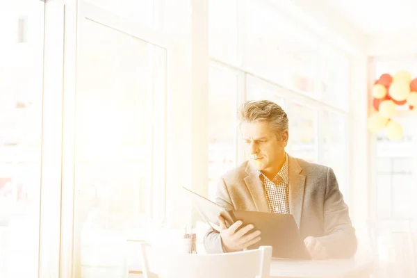 Mature customer sitting while looking on the menu in restaurant with yellow lens flare in background