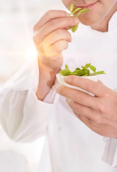 Mature Chef Smelling Herbs Bowl Kitchen Yellow Lens Flare Background — Stock Photo, Image