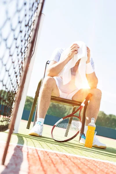 コートでプレーした後に座っている間にタオルで彼の汗を拭く成熟したテニス選手 — ストック写真