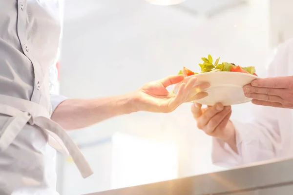 キッチンでお客様のために提供されるウェイターにサラダを与えるシェフ — ストック写真
