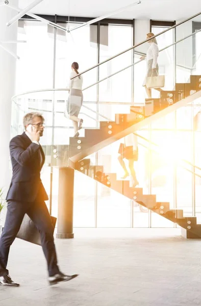 Mature Businessman Walking While Talking Smartphone Office Yellow Lens Flare — Stock Photo, Image