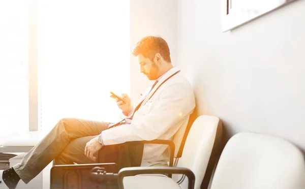 医生在诊所休息时用智能手机坐着 背景为黄色镜头照明弹 — 图库照片