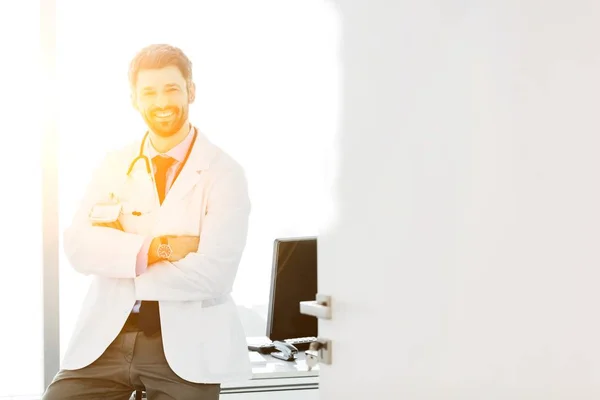 診療所で腕を組んで立っている間のハンサムな医者の笑顔の肖像画 — ストック写真