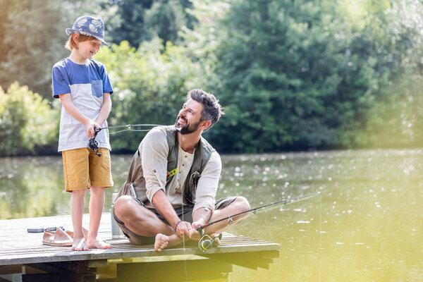 Father and son fishing in Lake while sitting on pier