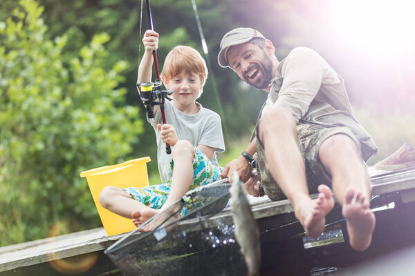 Father and son fishing in Lake while sitting on pier