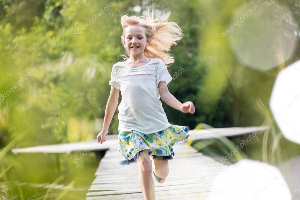 Smiling blond girl running on pier at lakeshore