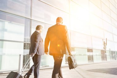 Olgun iş adamları havaalanında konuşurken yürüyorlar.