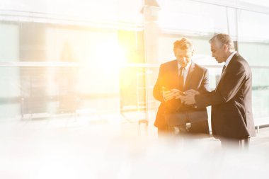 İş adamları havaalanında akıllı telefondan planlarını tartışıyor.