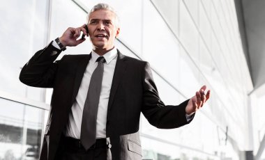 Olgun iş adamı havaalanında akıllı telefondan konuşuyor.