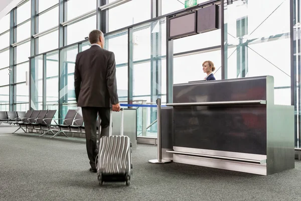 空港に搭乗するための彼のゲート上で彼のスーツケースと成熟したビジネスマンの歩行の後方ビュー — ストック写真