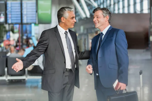 成熟的商人在机场与商业伙伴交谈时做手势 — 图库照片