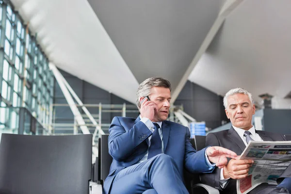 Mature Businessman Reading News Paper While Other Businessman Talking Smartphone — Stock Photo, Image