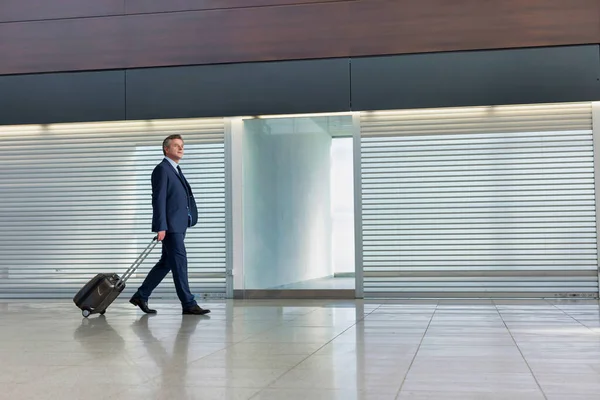 空港で彼のスーツケースと一緒に歩く成熟したビジネスマン — ストック写真