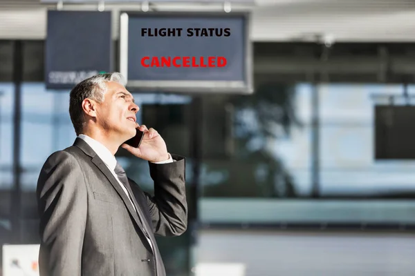Mature businessman making report on his cancelled flight while standing at his boarding gate in airport