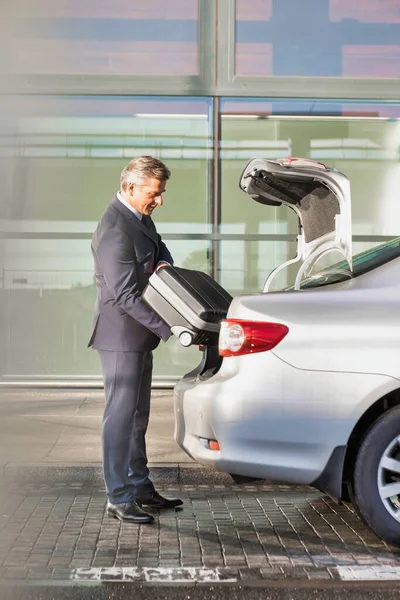 Çekici iş adamının portresi bavulunu bir arabanın bagajına koyuyor.