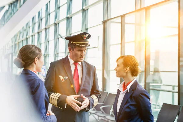 黄色のレンズフレアと空港で乗務員に話す成熟したパイロットの肖像 — ストック写真