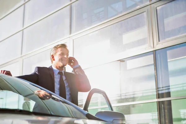 車の外に立っている間にスマートフォンで話して成熟した魅力的なビジネスマンの肖像画 — ストック写真