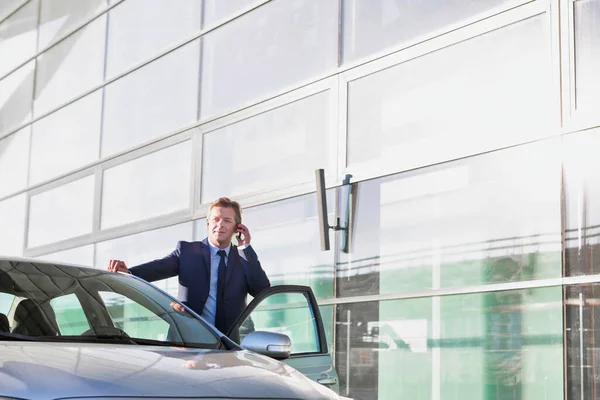車の外に立っている間にスマートフォンで話して成熟した魅力的なビジネスマンの肖像画 — ストック写真