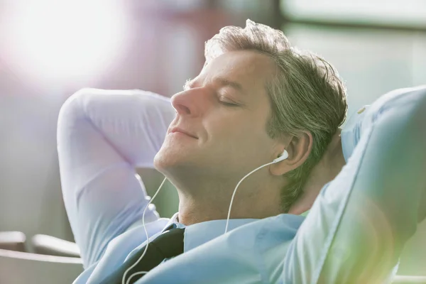 在机场 熟行的商人一边睡著 一边用耳机听着带有镜头照明弹的音乐 — 图库照片