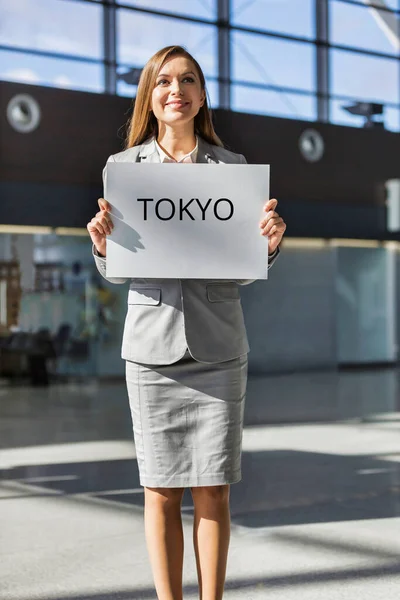 商务女性持白板站在机场抵达区持东京都交通标志的肖像 — 图库照片