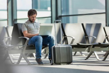 Havaalanında yolcu beklerken dizüstü bilgisayarıyla çalışan adamın portresi.