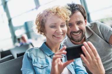 Yetişkin bir çiftin havaalanında beklerken selfie çekerken ve seyrederken portresi.