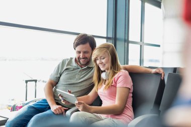 Havalimanında oturup uçuşlarını beklerken babasına dijital tablet gösteren güzel bir genç kızın portresi.