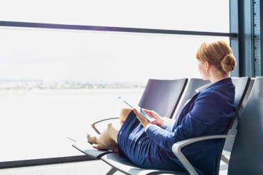 Genç ve güzel havaalanı çalışanları tatilde sandalyede otururken dijital tablet kullanıyorlar.