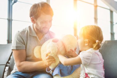 Havaalanında oturup beklerken kızıyla oynayan bir adamın portresi.