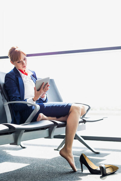 Young beautiful airport staff using digital tablet while sitting on chair during break