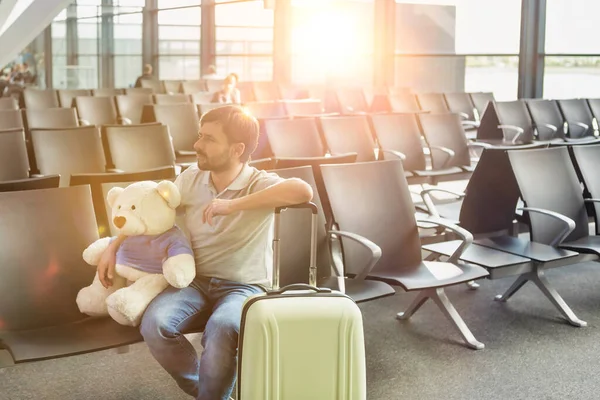 空港で搭乗を待っている間にテディベアとスーツケースと座っている男の肖像画 — ストック写真