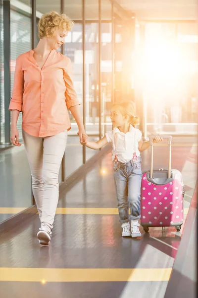 成熟した女性の肖像画彼女の娘と一緒に空港の到着エリアにレンズフレアで歩く — ストック写真