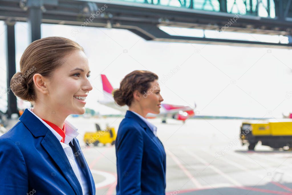 Photo of confident flight attendants walking against airplane in airport