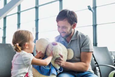 Havaalanında oturup beklerken kızıyla oynayan bir adamın portresi.