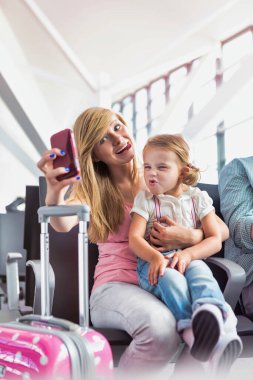 Havaalanında beklerken küçük kız kardeşiyle selfie çeken genç kızın portresi.