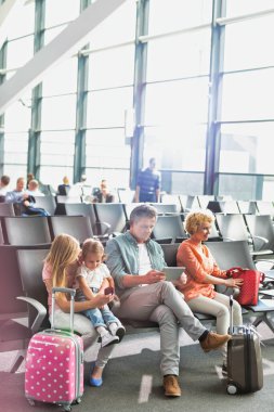 Olgun adam, karısı ve kızı havaalanında ararken dijital tablet kullanıyor.