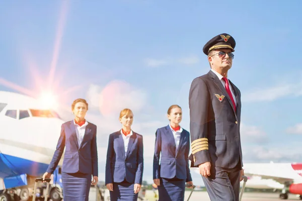 大人のパイロットの肖像空港で飛行機に対して3人の若い美しい客室乗務員と歩く — ストック写真
