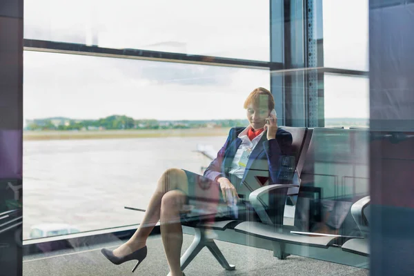 スマホで話しながら座っている若い魅力的な空港スタッフの写真 — ストック写真