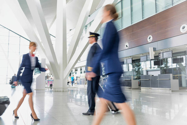 Mature pilot with young beautiful flight attendants walking in airport