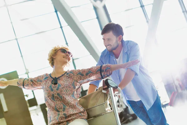 Man Skjuter Bagagevagn För Incheckning Medan Hans Fru Sitter Flygplatsen — Stockfoto