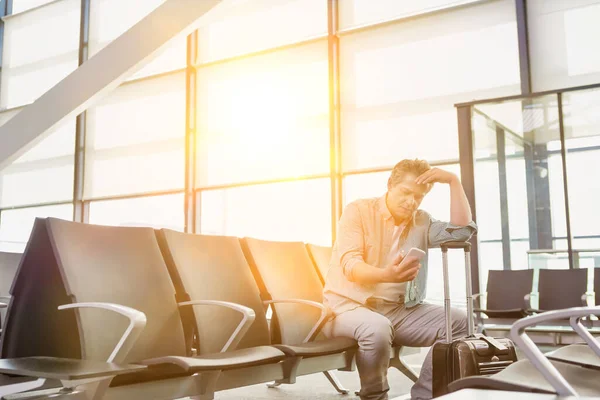 空港で彼の携帯電話を見ている間に座ってストレス成熟した男の写真 — ストック写真