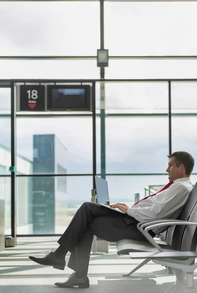成熟商人坐在笔记本电脑上等待机场航班时的肖像 — 图库照片
