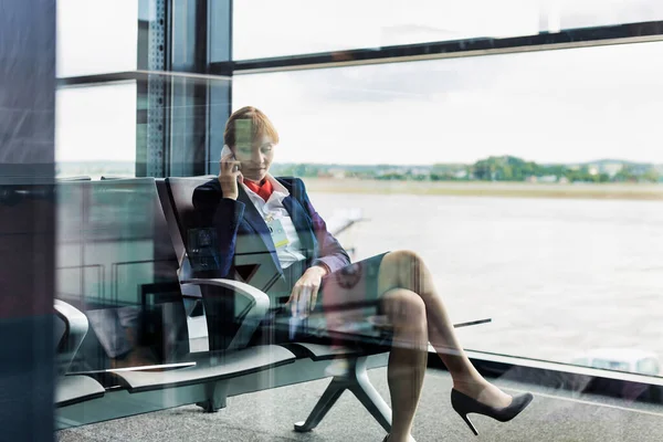 スマホで話しながら座っている若い魅力的な空港スタッフの写真 — ストック写真