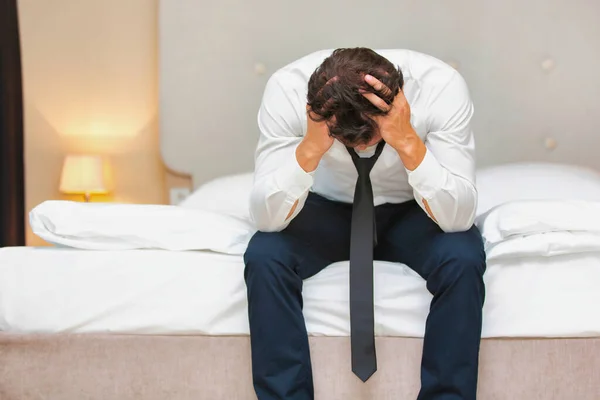 過労とストレスの多いビジネスマンがベッドの上に座って — ストック写真