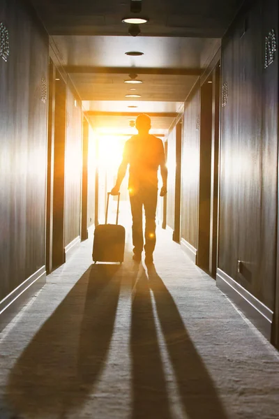 ホテルでスーツケースと一緒に歩く男のリアビュー — ストック写真