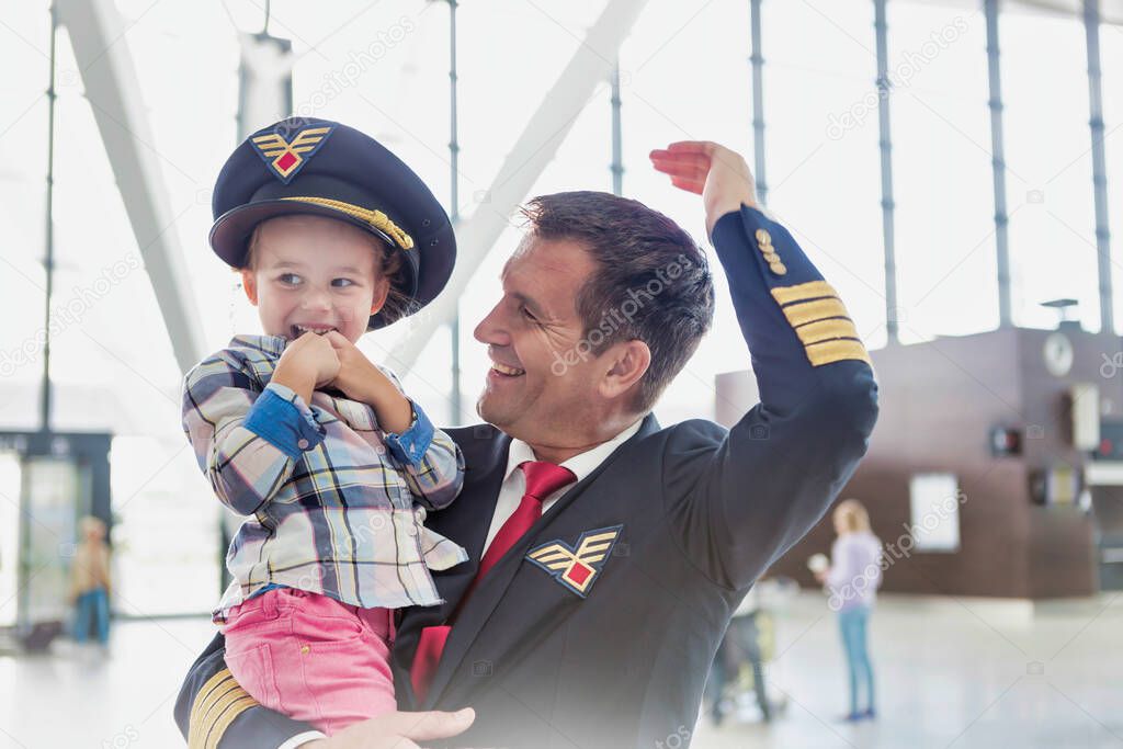 Portrait of mature pilot carrying cute little child in airport