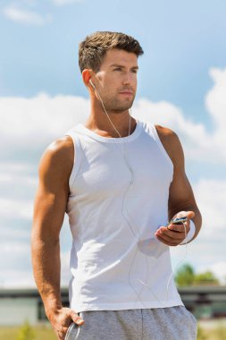 Parkta akıllı telefonuyla müzik dinlerken ayakta duran çekici bir adamın portresi.