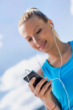 Parkta akıllı telefonuyla müzik dinlerken ayakta duran çekici bir kadının portresi.