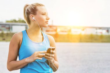 Parkta akıllı telefonuyla müzik dinlerken ayakta duran çekici bir kadının portresi.