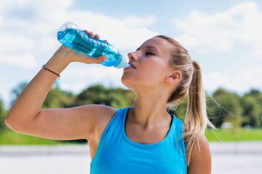 Parkta enerji içeceği içen çekici genç bir kadının portresi.